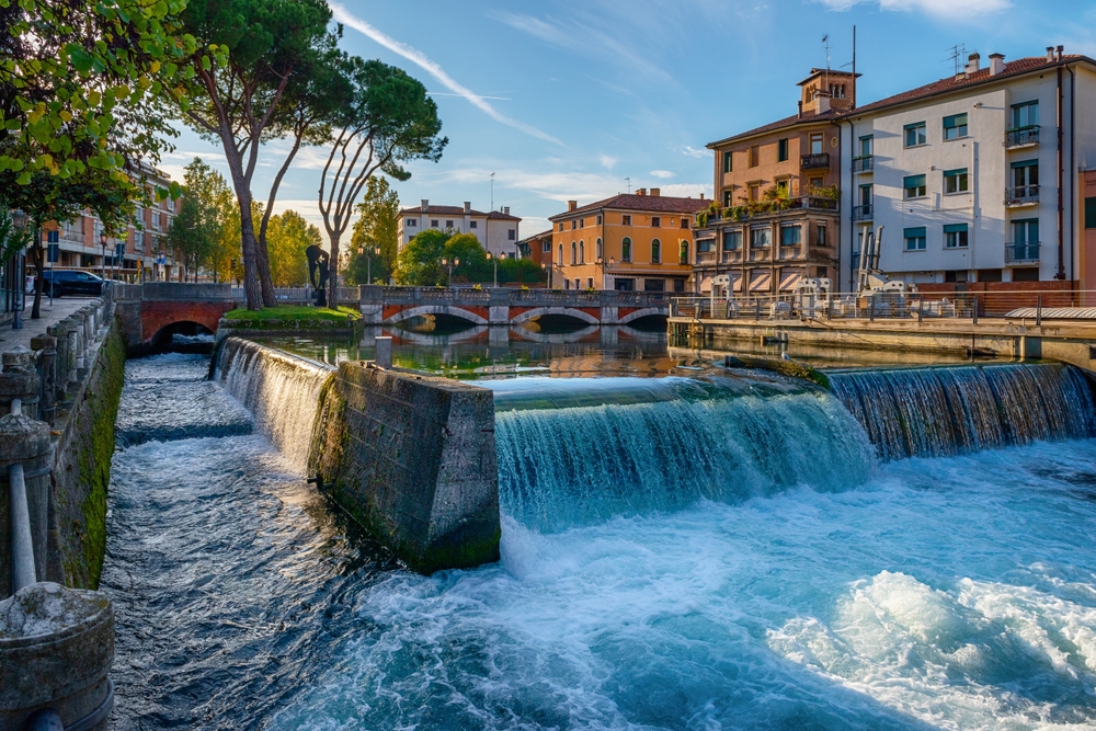 Jaz na rzece Sile w Treviso wieczorem, spieniona woda i most San Martino w tle