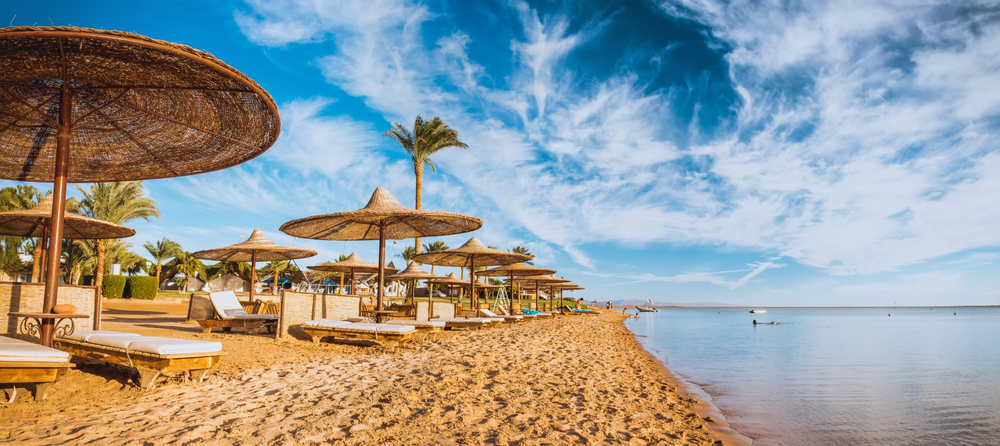 Plaża w Hurghadzie ze słomianymi parasolami i palmami nad brzegiem