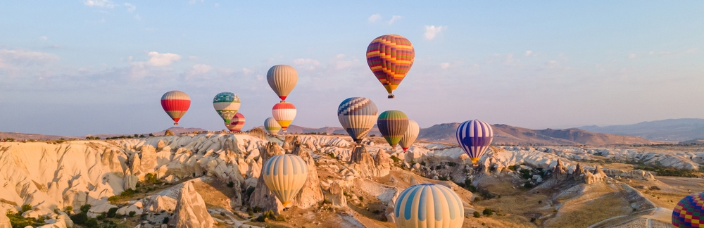Kolorowe balony na ogrzane powietrze unoszące się nad skalistym krajobrazem Kapadocji o świcie