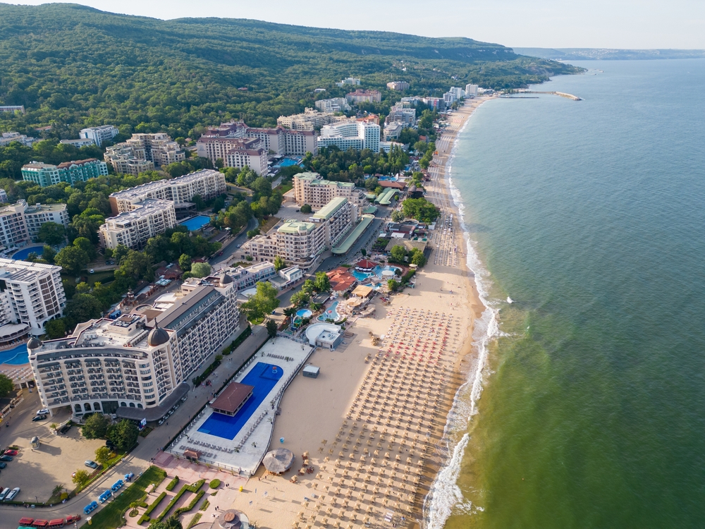 Plaża Złote Piaski z drobnym żółtym piaskiem i zielonymi wzgórzami parku przyrodniczego w tle
