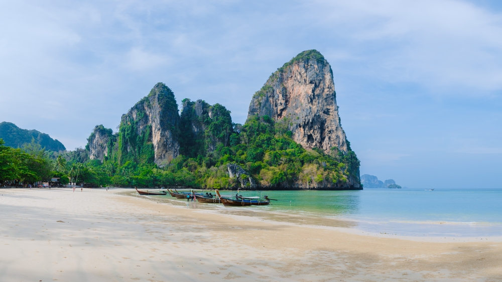 Plaża Railay West z łodziami longtail u podnóża wapiennych klifów
