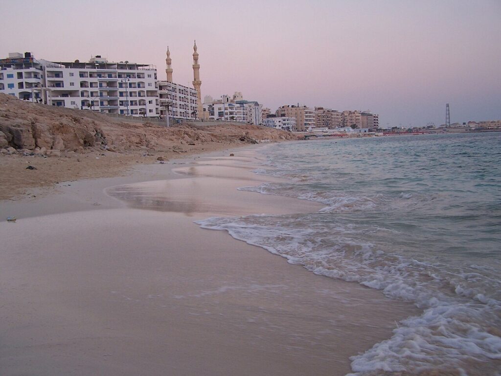 Plaża miejska w Marsa Matruh o zmierzchu, biały piasek i minarety meczetu nad linią zabudowy