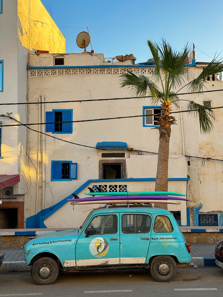 Stary Renault 4 z deskami surfingowymi na dachu przed szkołą surfingu w Taghazout