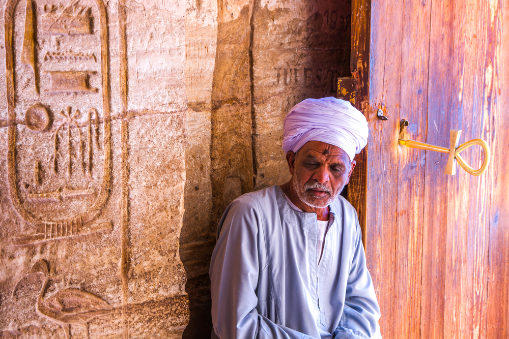 Mężczyzna w turbanie siedzący przy drewnianych drzwiach świątyni w Abu Simbel, obok kartusz z hieroglifami