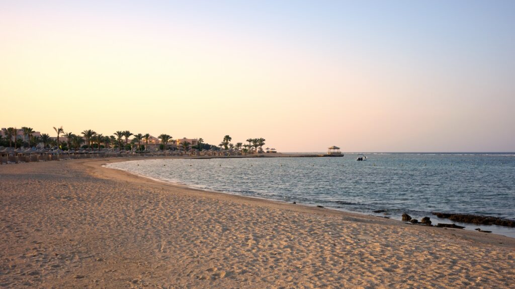 Pusta piaszczysta plaża w Marsa Alam o zachodzie słońca, palmy i pomost nad wodą
