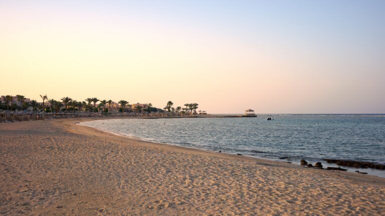 Pusta piaszczysta plaża w Marsa Alam o zachodzie słońca, palmy i pomost nad wodą
