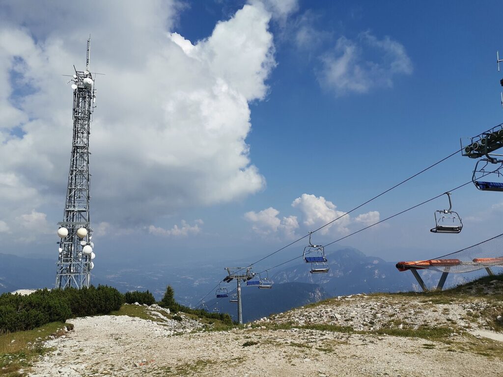 Maszt z antenami i kanapa na Cima Paganella latem, w tle pasma gór