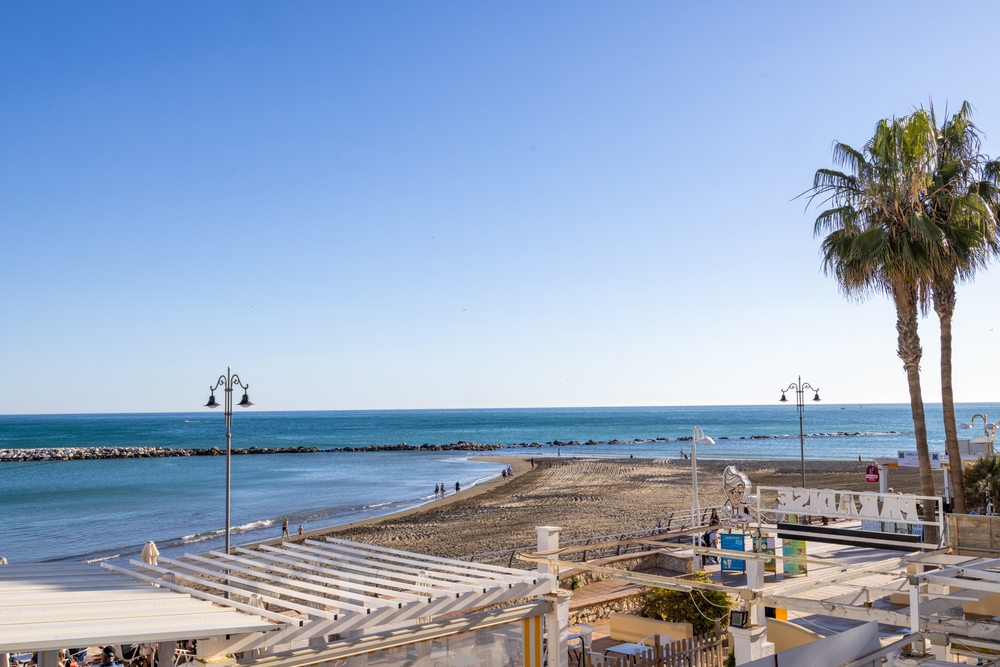 Plaża w Benalmádenie z falochronami, biała pergola i palma nad promenadą