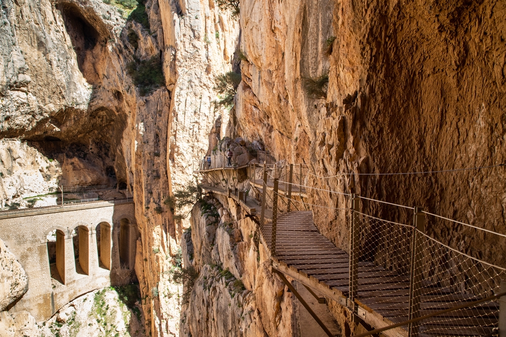 Drewniana kładka Caminito del Rey nad wąwozem, obok resztki starej ścieżki i wiadukt