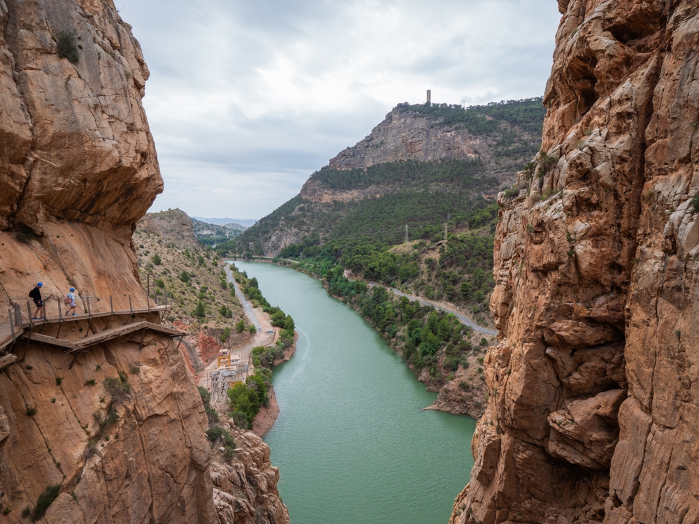 Widok z kładki Caminito del Rey na zieloną rzekę w dolinie i wzgórze z wieżą na szczycie