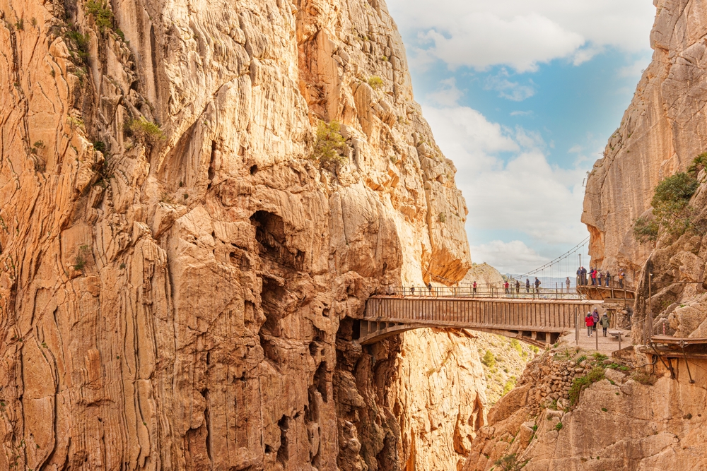 Most i kładka Caminito del Rey wśród jasnych skał, grupa turystów na przejściu