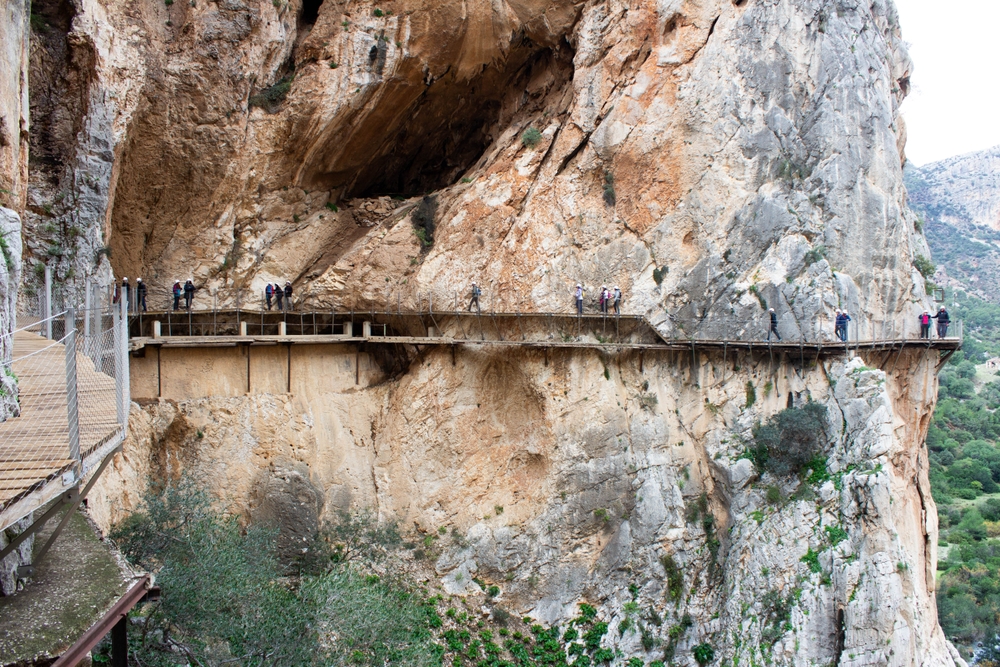 Długa kładka Caminito del Rey przyklejona do ściany wąwozu, turyści idący jeden za drugim