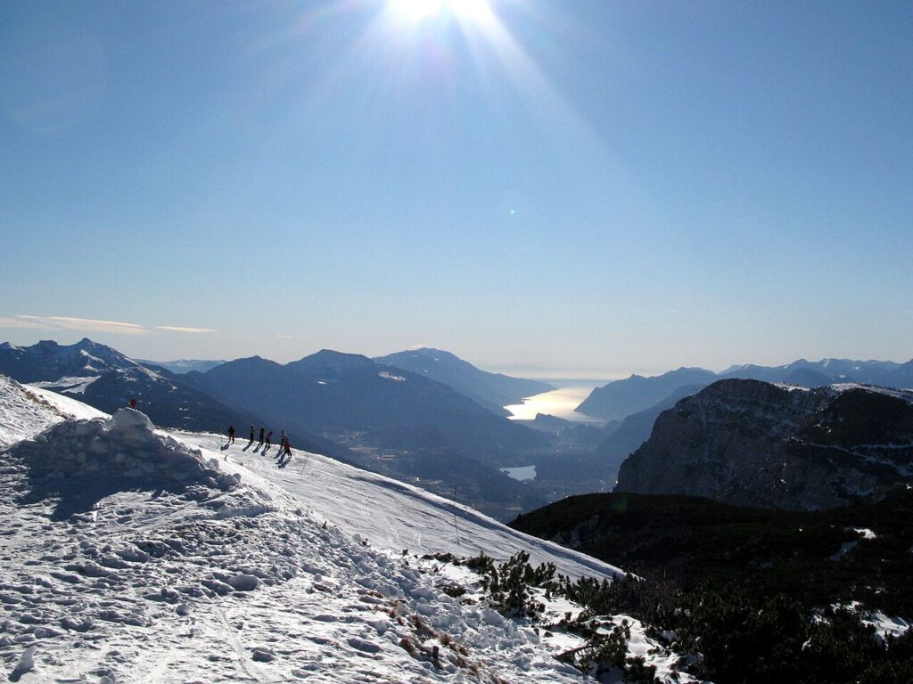 Narciarze na grani Cima Paganella, w dole doliny z jeziorami Molveno i Garda