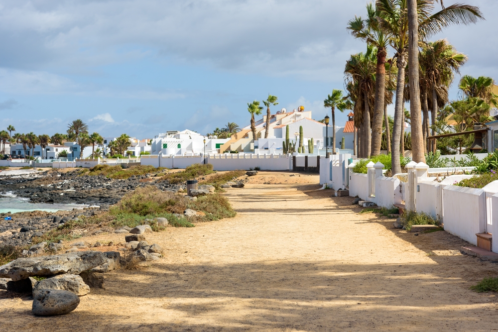 Nadmorska ścieżka spacerowa w Corralejo wśród palm i białych domów nad skalistym brzegiem