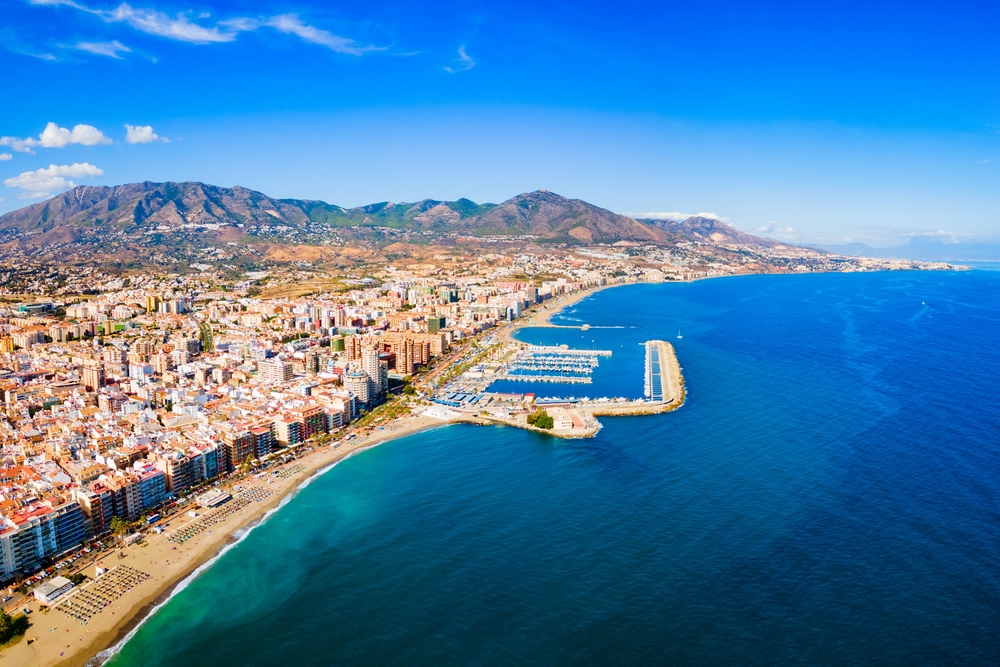 Fuengirola z lotu ptaka, długa plaża, marina z falochronem i pasmo gór za miastem