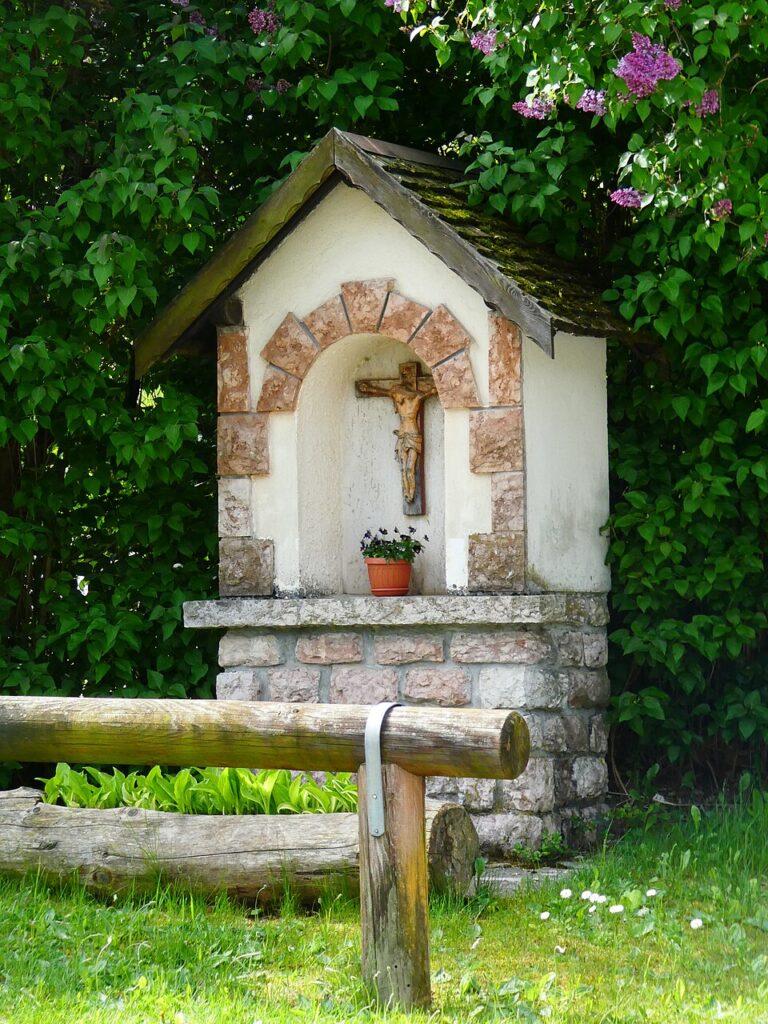 Kapliczka z krucyfiksem przy Via Risorgimento w Fai della Paganella, wśród bzu