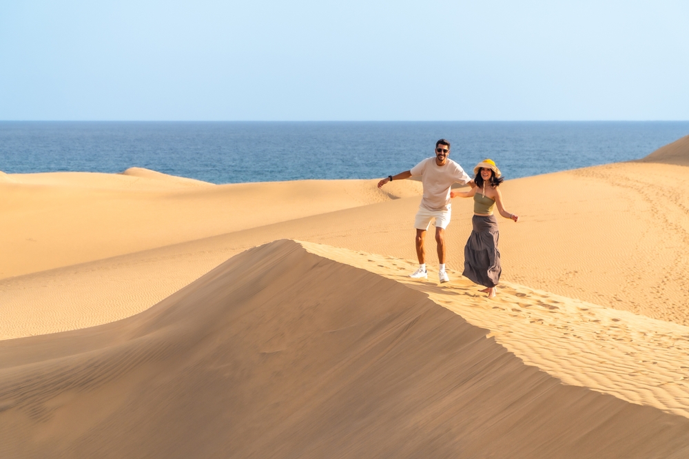 Dwie osoby zbiegające ze zbocza wydmy w Maspalomas, w tle Atlantyk