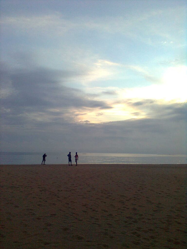 Sylwetki spacerowiczów na płyciźnie plaży Pasikudah pod pochmurnym niebem