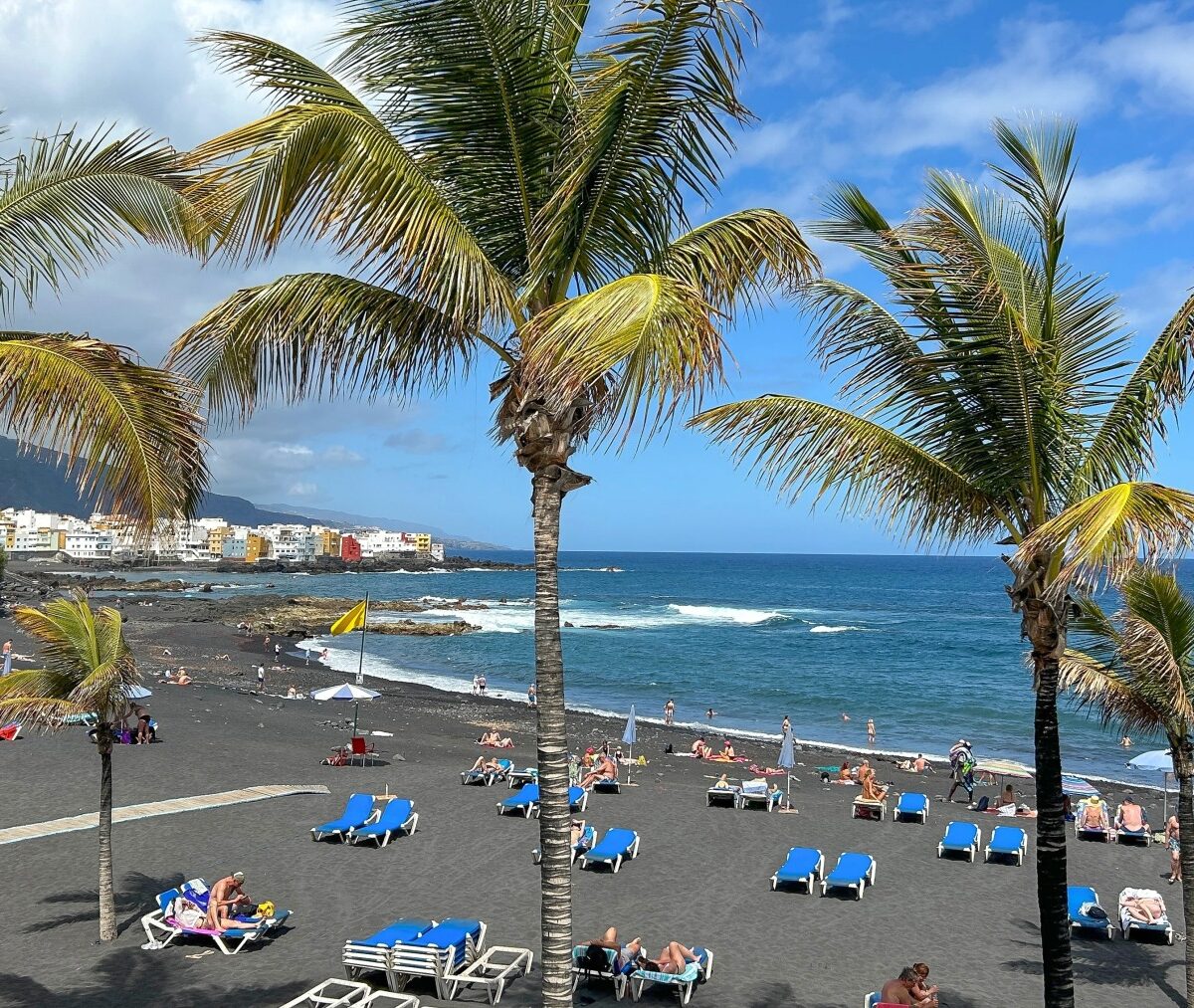 Plaża z ciemnym piaskiem w Puerto de la Cruz, palmy i parasole nad oceanem