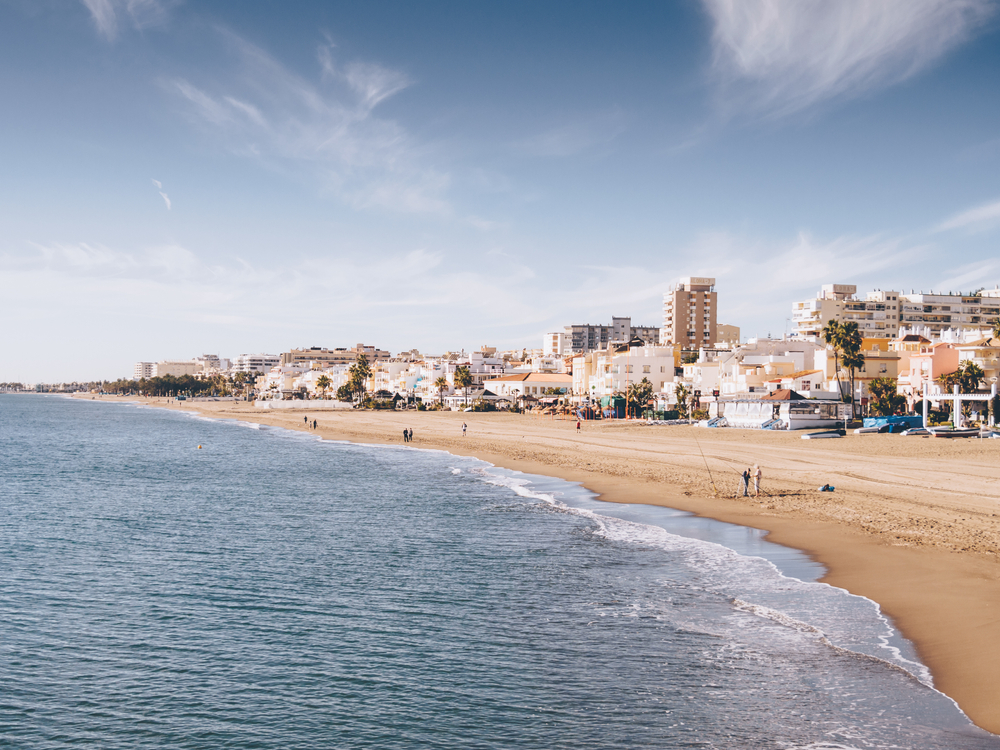 Szeroka plaża w Torremolinos o poranku, fala przy brzegu i zabudowa kurortu