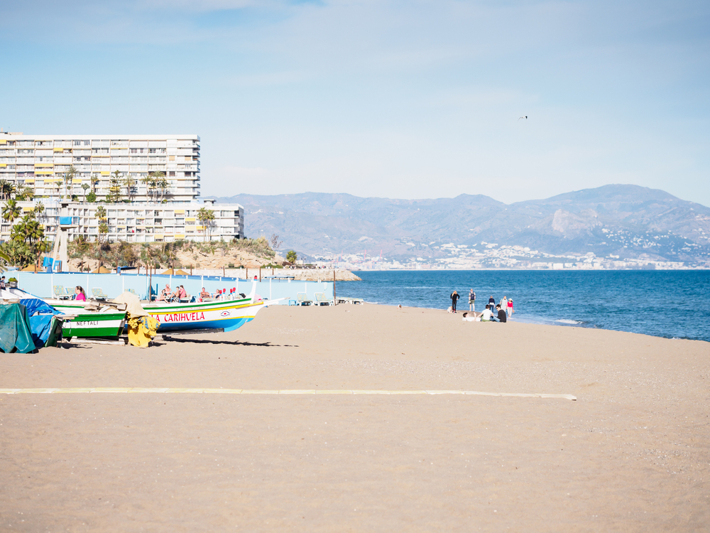Plaża La Carihuela w Torremolinos, kolorowe łodzie na brzegu i góry nad zatoką