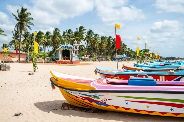 Kolorowe łodzie rybackie na piasku plaży w Trincomalee, w tle palmy i kapliczka