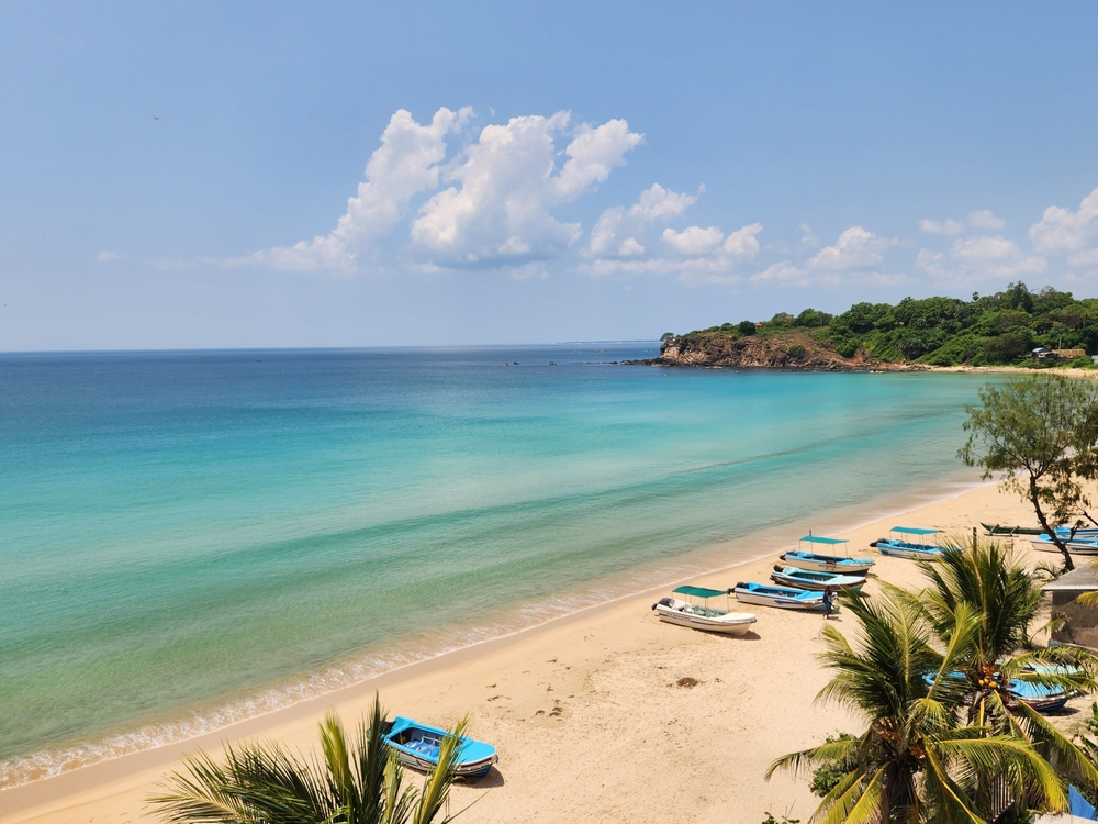 Turkusowa zatoka z łódkami na plaży pod zalesionym cyplem w Trincomalee