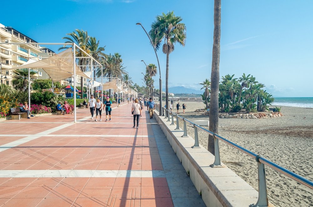 Promenada nadmorska w Esteponie, spacerowicze pod palmami i plaża po prawej stronie