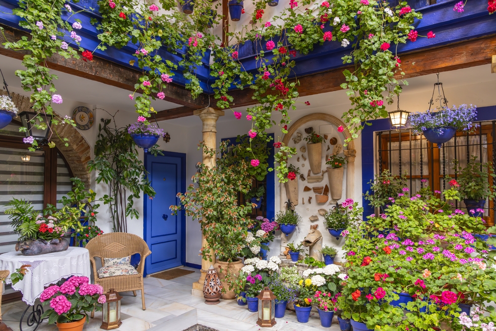 Patio w Kordobie pełne doniczek z pelargoniami, niebieskie drzwi i kamienna kolumna pośrodku