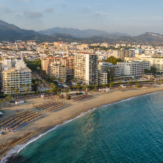 Marbella z lotu ptaka, łuk plaży z leżakami i pasmo gór za miastem