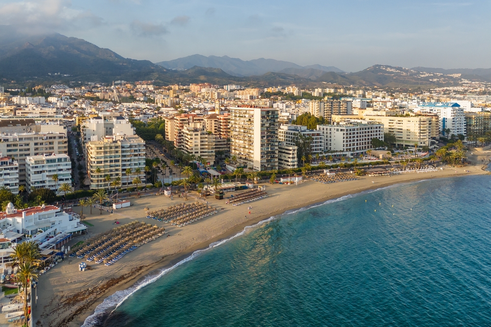 Marbella z lotu ptaka, łuk plaży z leżakami i pasmo gór za miastem