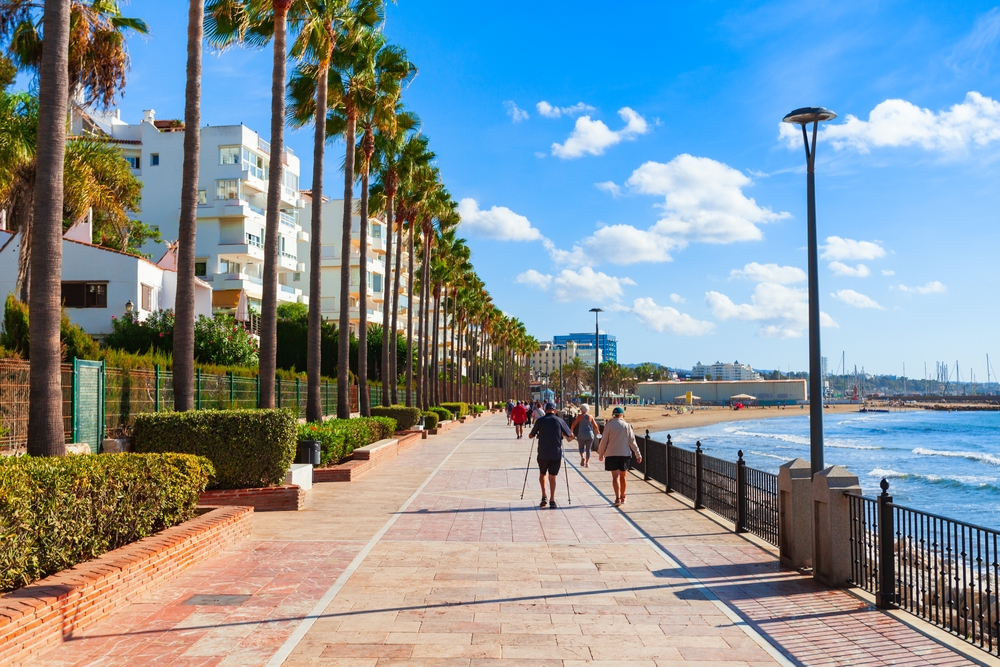 Aleja palm wzdłuż promenady w Marbelli, spacerowicze i plaża po prawej stronie