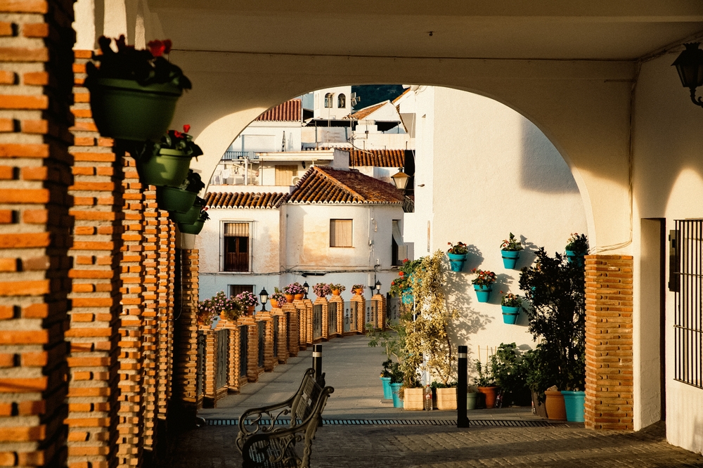 Przejście pod arkadą w Mijas Pueblo, donice na murku i bielone domy w popołudniowym słońcu
