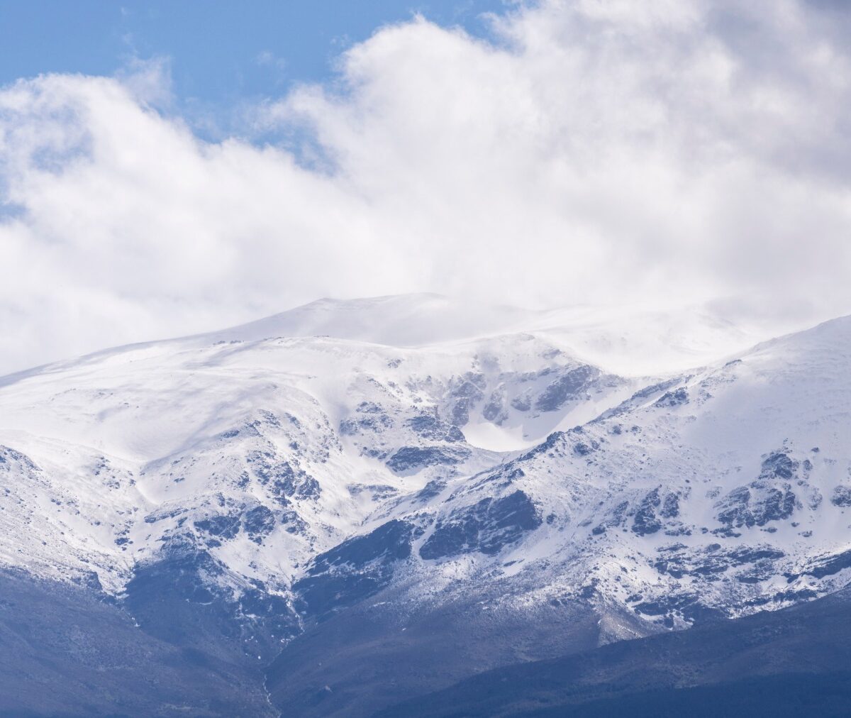 Ośnieżony grzbiet Sierra Nevady w chmurach, poniżej ciemne zbocza bez śniegu