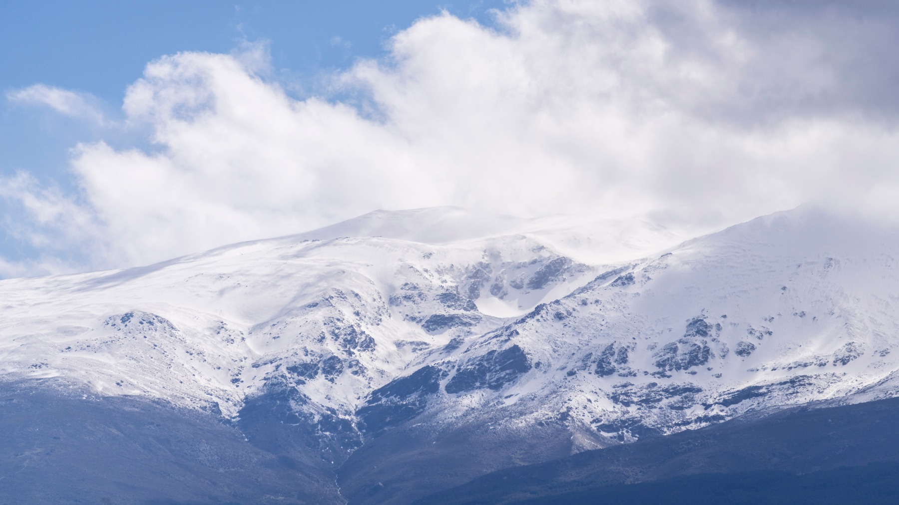 Ośnieżony grzbiet Sierra Nevady w chmurach, poniżej ciemne zbocza bez śniegu