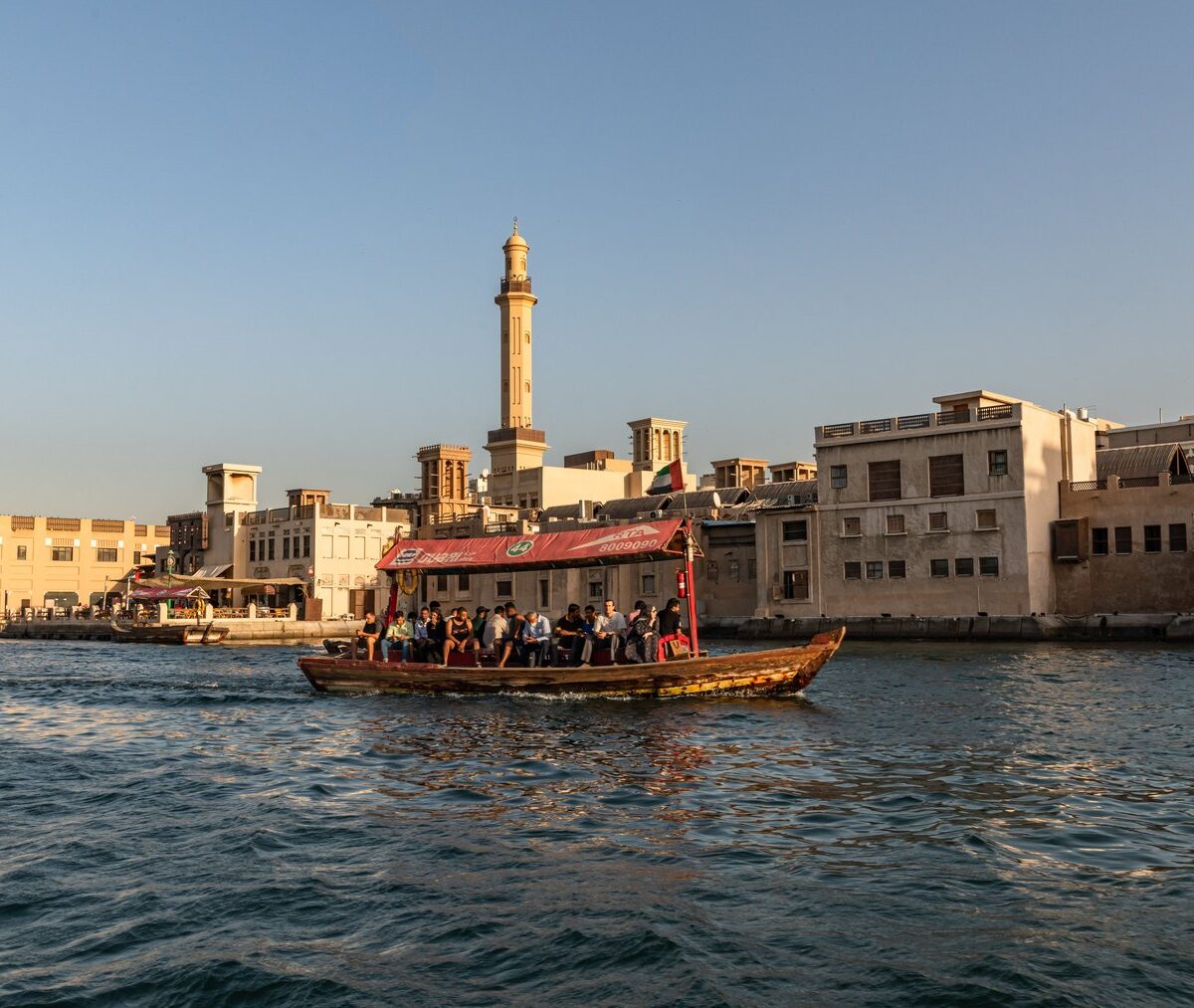 Drewniana abra z pasażerami płynie przez Dubai Creek na tle starego miasta Bur Dubaj