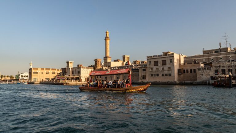 Drewniana abra z pasażerami płynie przez Dubai Creek na tle starego miasta Bur Dubaj