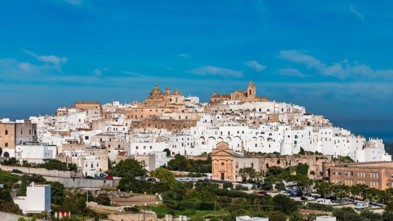 Białe stare miasto Ostuni na wzgórzu z katedrą na szczycie, poniżej zieleń i niebieskie niebo