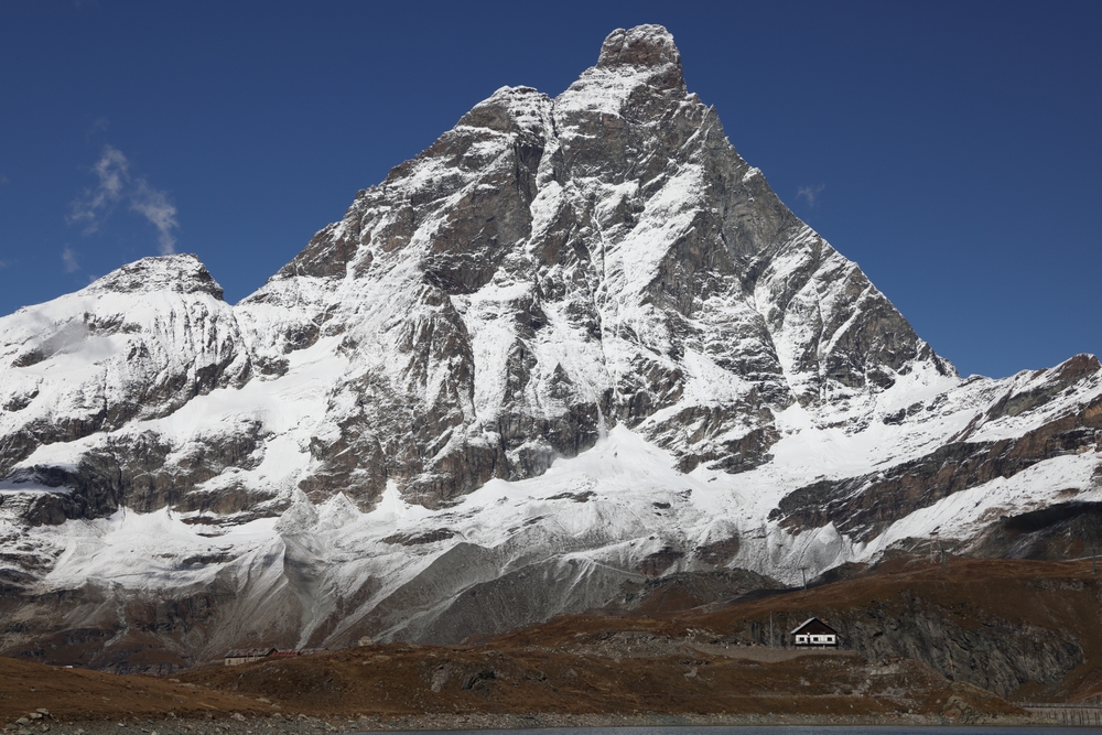 Matterhorn od strony włoskiej jesienią, przyprószony śniegiem, z małym schroniskiem u podnóża
