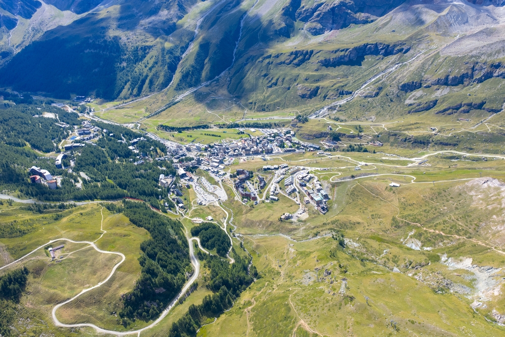 Breuil-Cervinia z lotu ptaka latem, zabudowa na zielonym płaskowyżu i serpentyny drogi z doliny