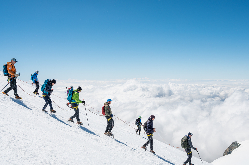 Grupa alpinistów związana liną schodzi po śnieżnym grzbiecie nad morzem chmur