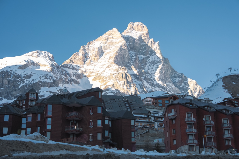 Matterhorn w porannym słońcu nad ceglastymi apartamentowcami Cervinii, na stoku po prawej wyciąg