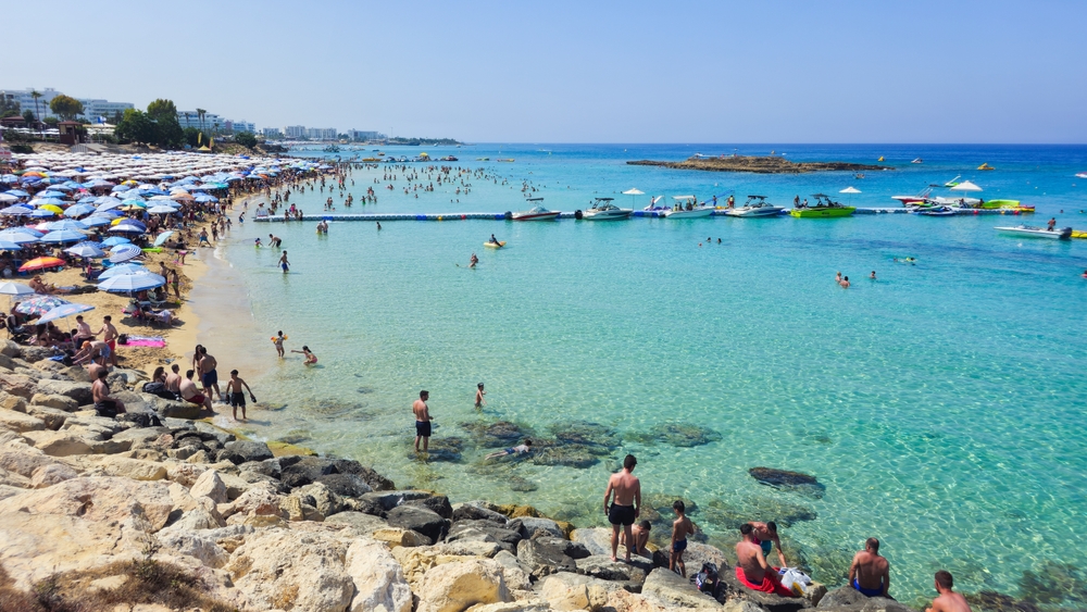 Plażowicze na Fig Tree Bay w Protaras, parasole na piasku i wysepka na horyzoncie