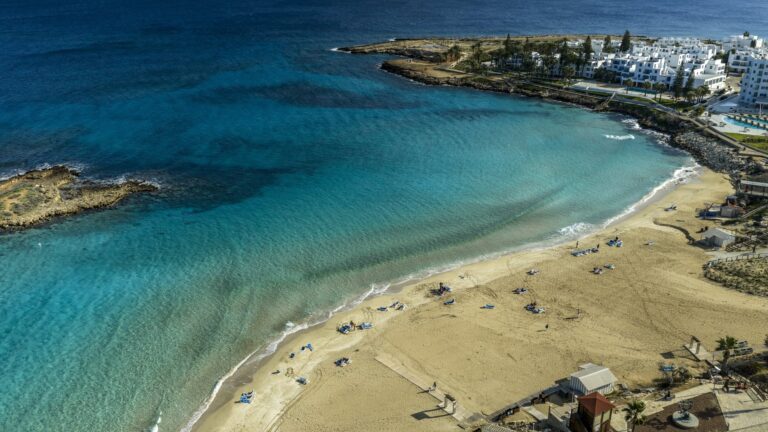 Fig Tree Bay w Protaras z drona, piaszczysta plaża, turkusowa woda i wysepka w zatoce