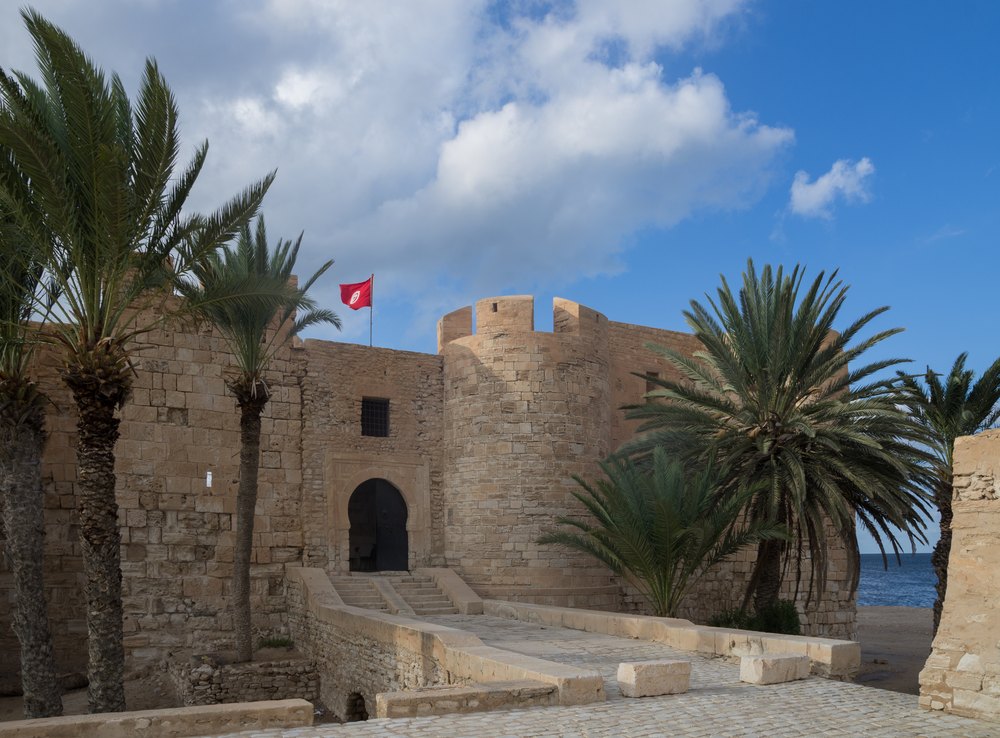 Kamienny fort Borj el Kebir w Houmt Souk z basztą i bramą wśród palm, w tle morze