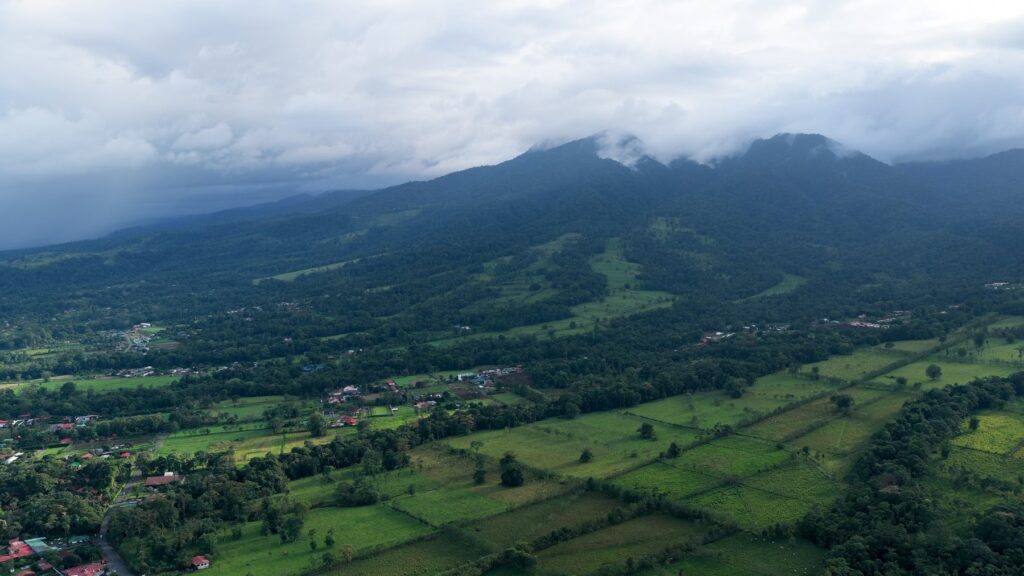 Zalesione góry w chmurach nad polami i domami w okolicy La Fortuny w Kostaryce