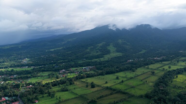 Zalesione góry w chmurach nad polami i domami w okolicy La Fortuny w Kostaryce