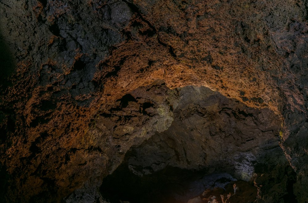 Oświetlony korytarz tunelu lawowego Gruta do Natal z rdzawymi ścianami zastygłej lawy