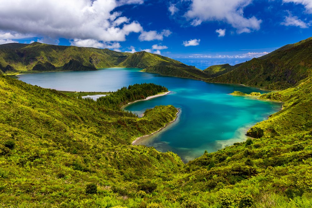 Turkusowe jezioro Lagoa do Fogo w kraterze otoczonym zielonymi zboczami, przy brzegu piaszczysta mierzeja