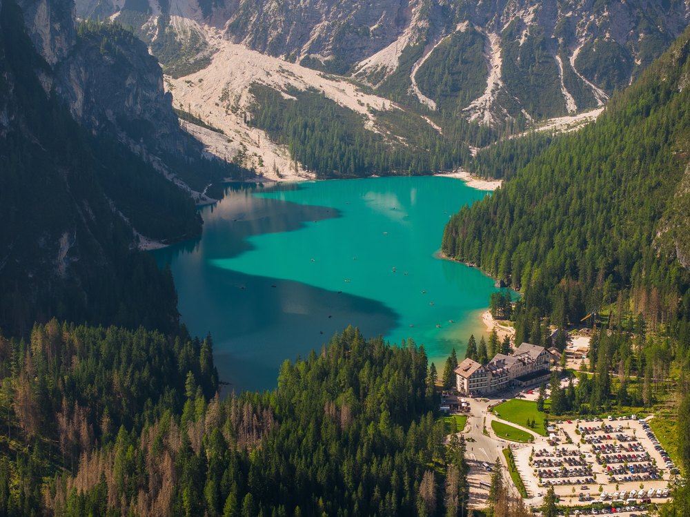Lago di Braies z lotu ptaka, turkusowa woda w leśnej dolinie, przy brzegu hotel i parking
